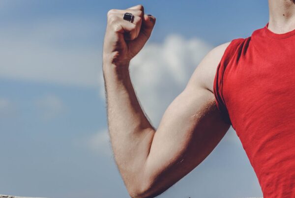 Healthy muscular arm flexing under blue sky, representing strong health for life insurance